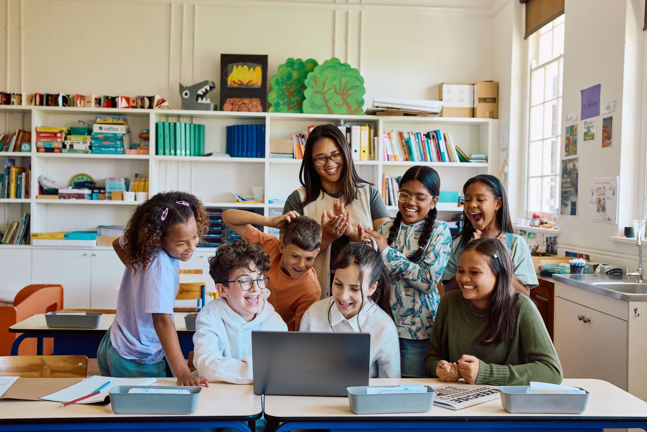 Teacher and school children smiling together around a laptop in a classroom